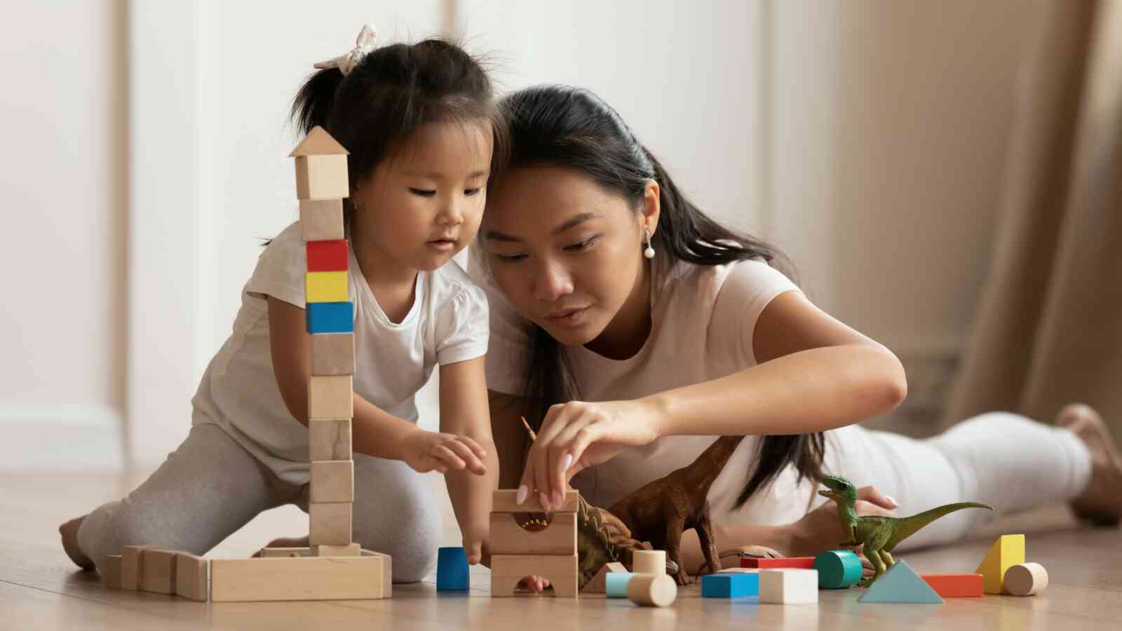 A young child and an adult female are sitting next to each other stacking blocks. Both individuals have light brown skin